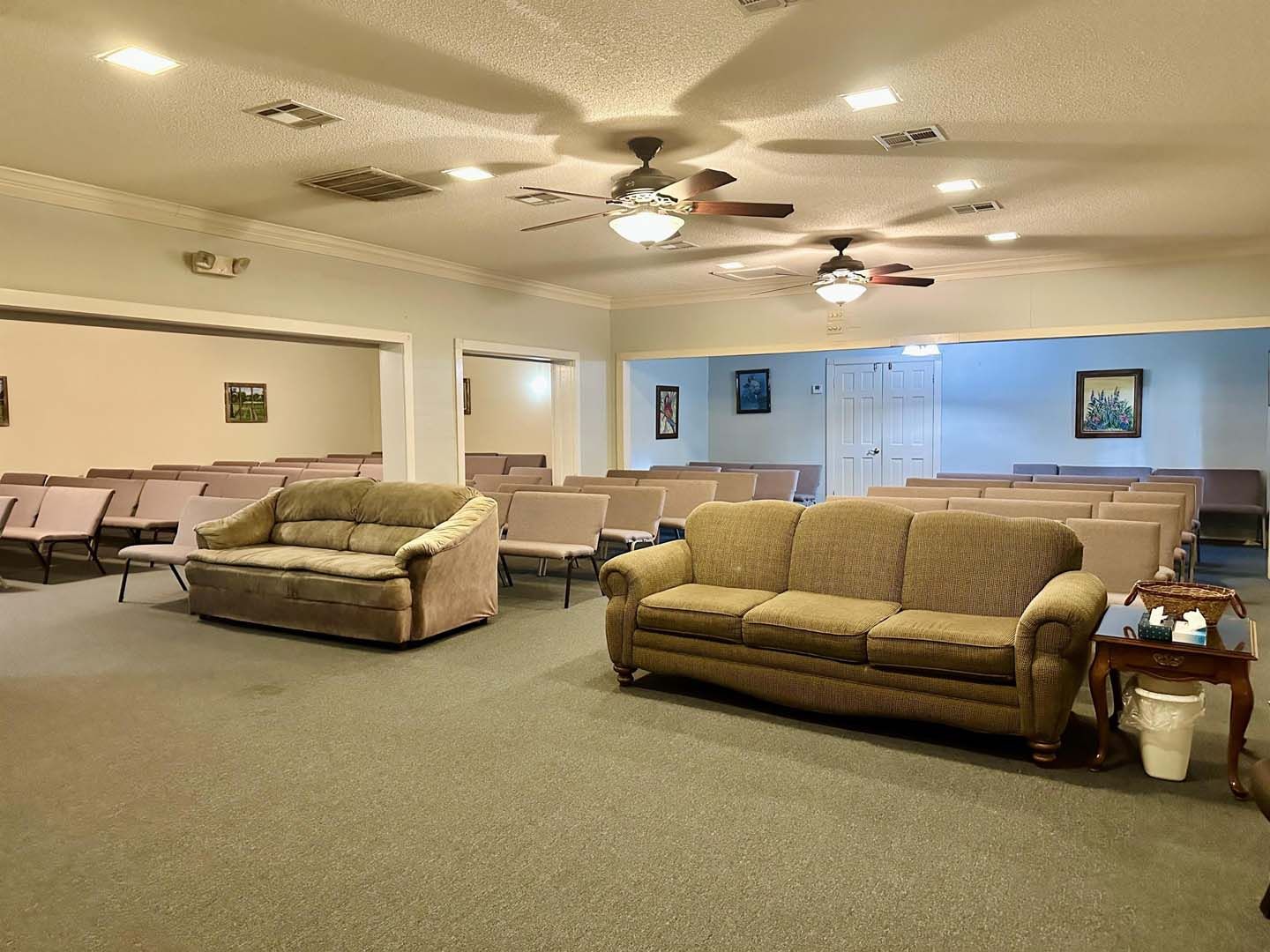 A room with rows of chairs, sofas, and ceiling fans.