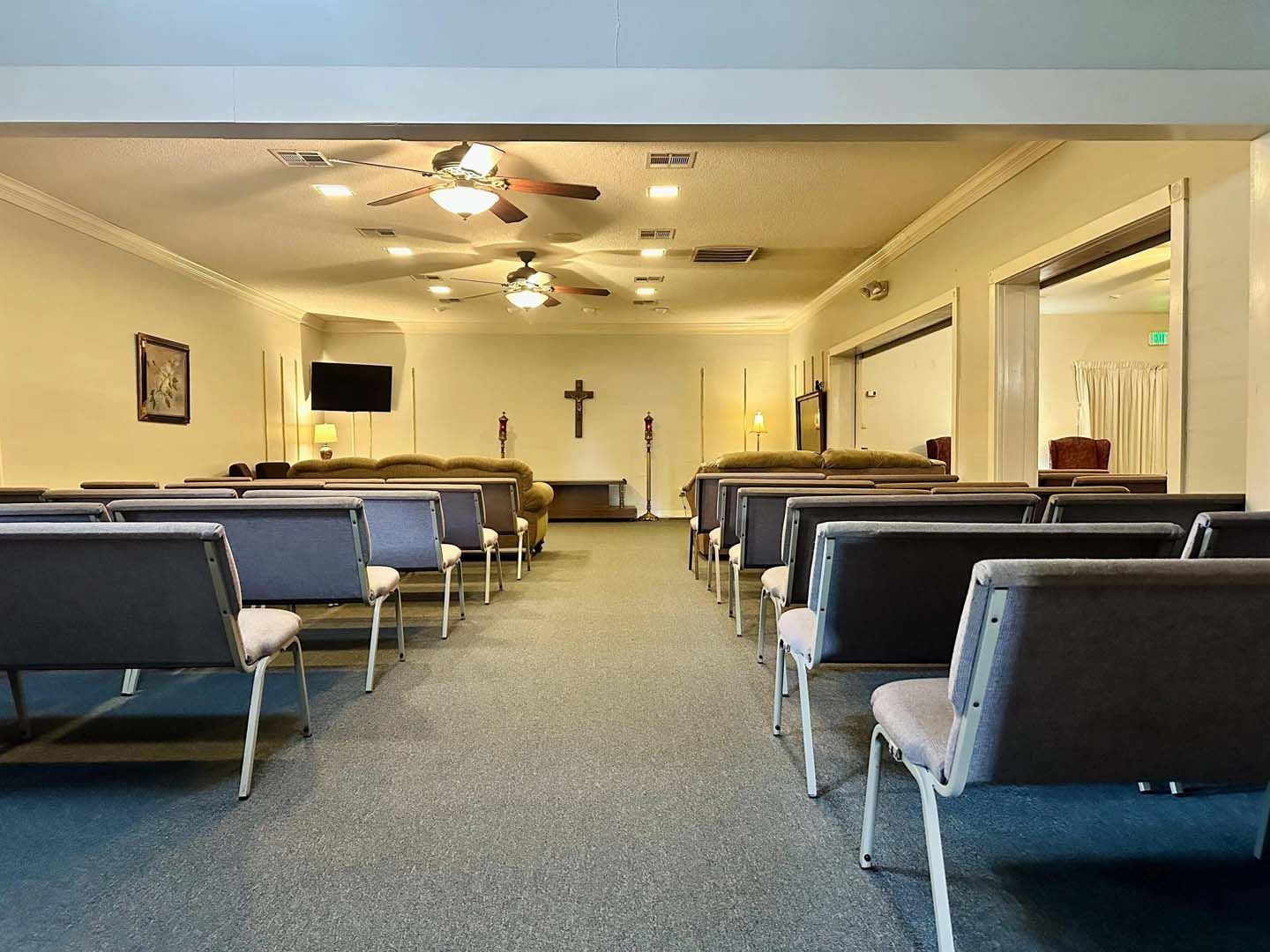 Interior of a funeral home chapel with rows of chairs, a cross, and ceiling fans.