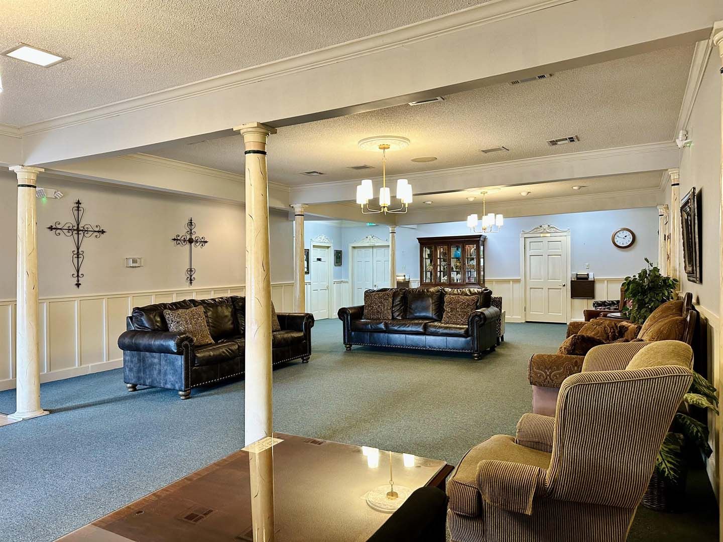 Spacious room with couches and armchairs. Columns support the ceiling. Crosses hang on the wall.