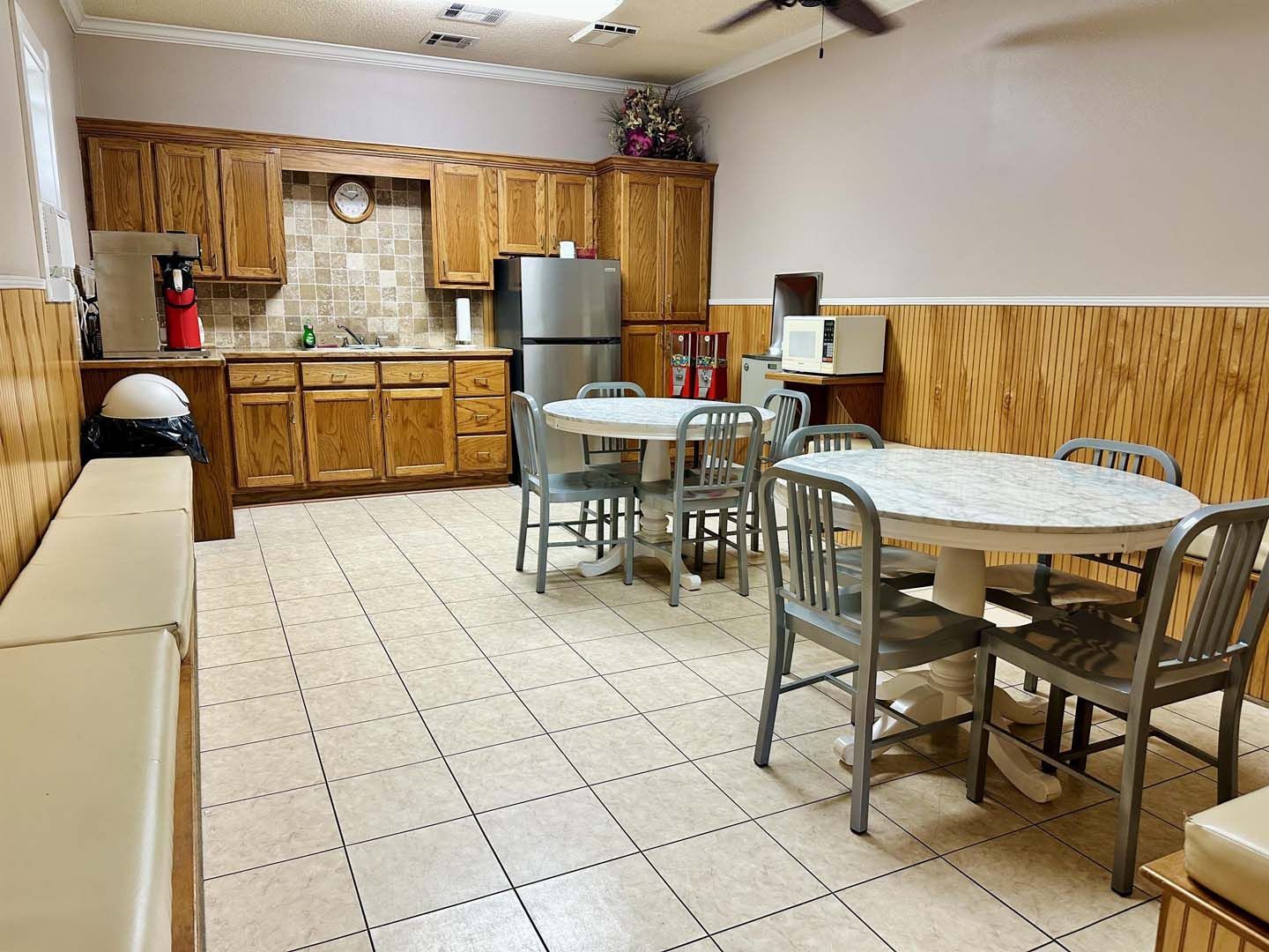 Kitchen area with wood cabinets, tiled floor, tables, chairs, and refrigerator.