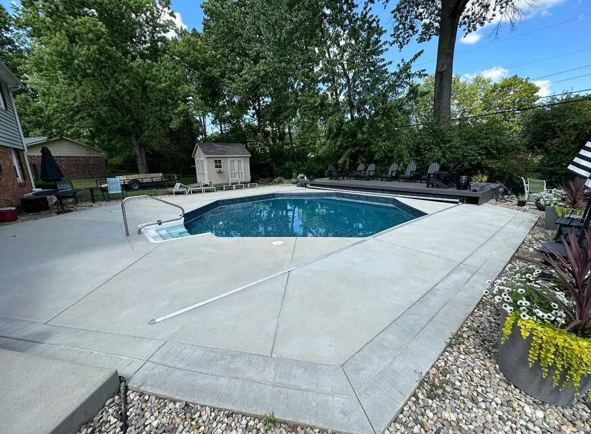 Backyard with a dark blue, octagonal swimming pool surrounded by concrete and landscaping.