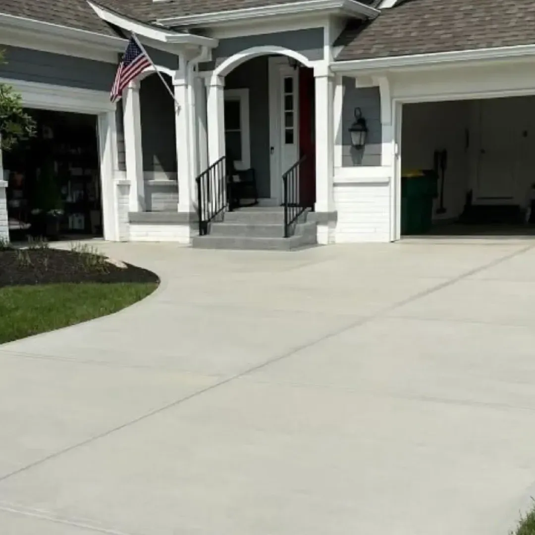 Concrete driveway leading to a house with a porch and garage. American flag visible.