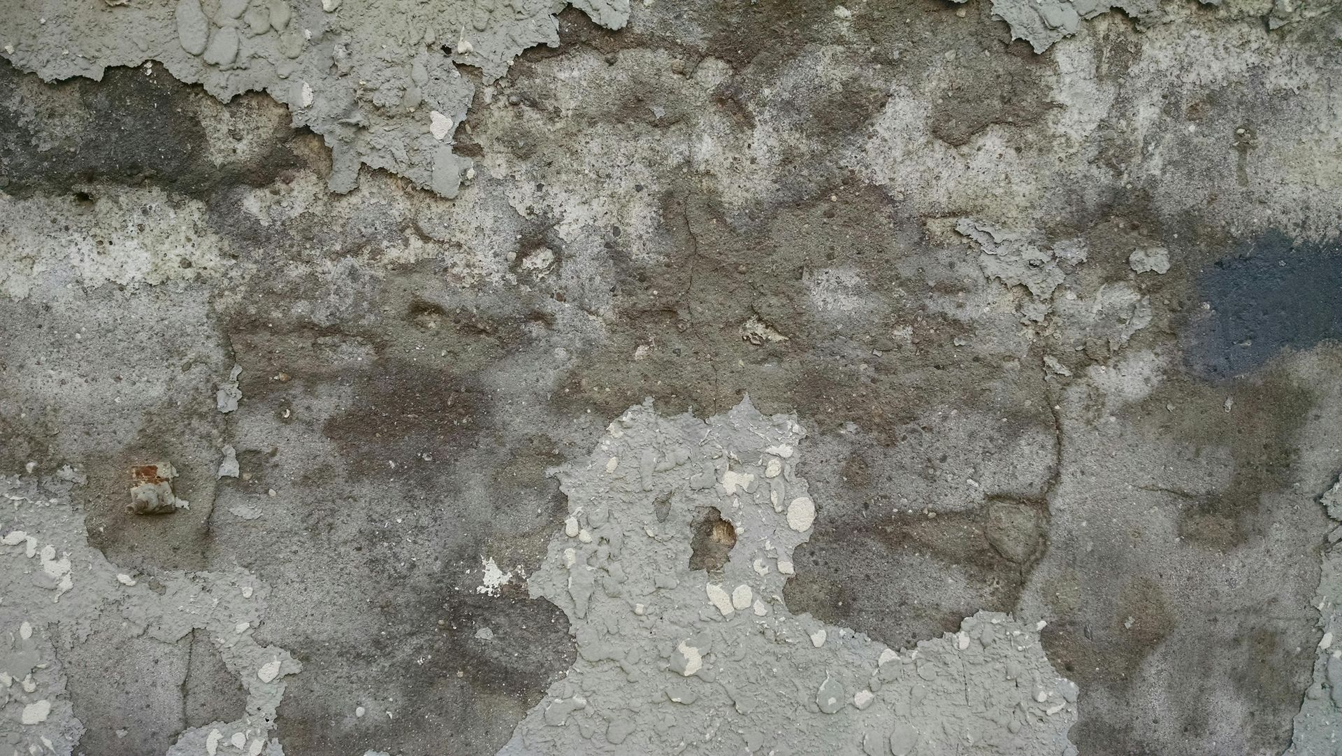 Rough gray concrete wall with peeling patches and weathered texture