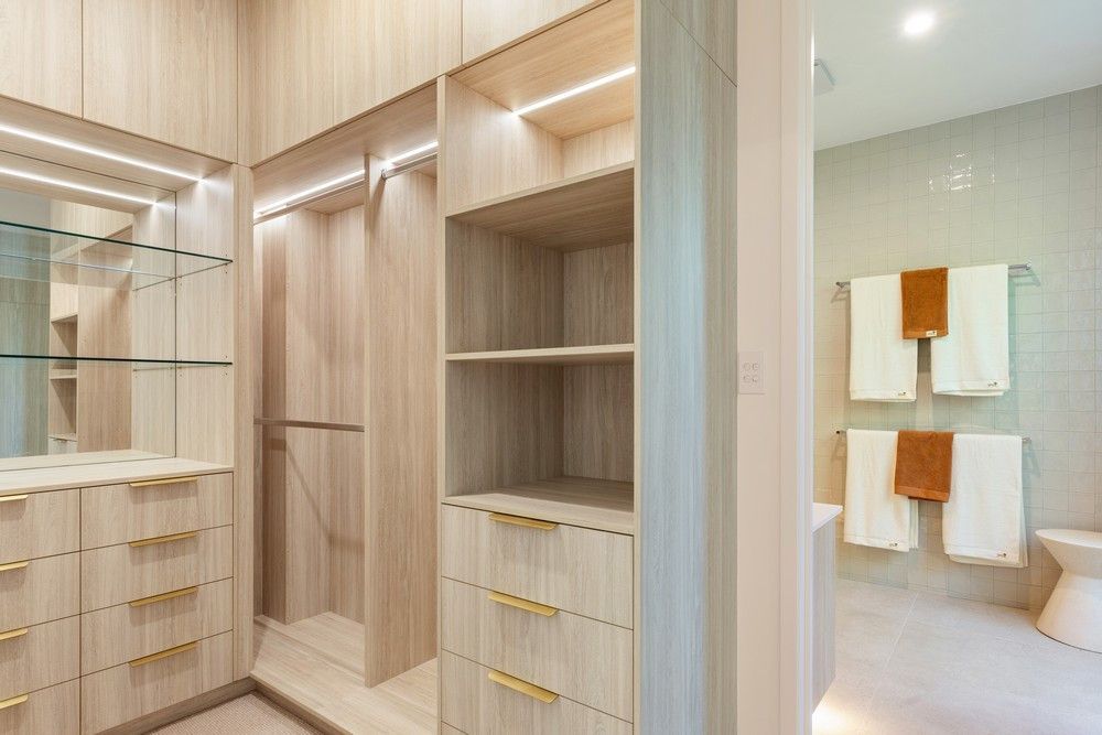 A walk in closet with wooden cabinets and drawers next to a bathroom — Kitchens by CCJS in Bungalow, QLD