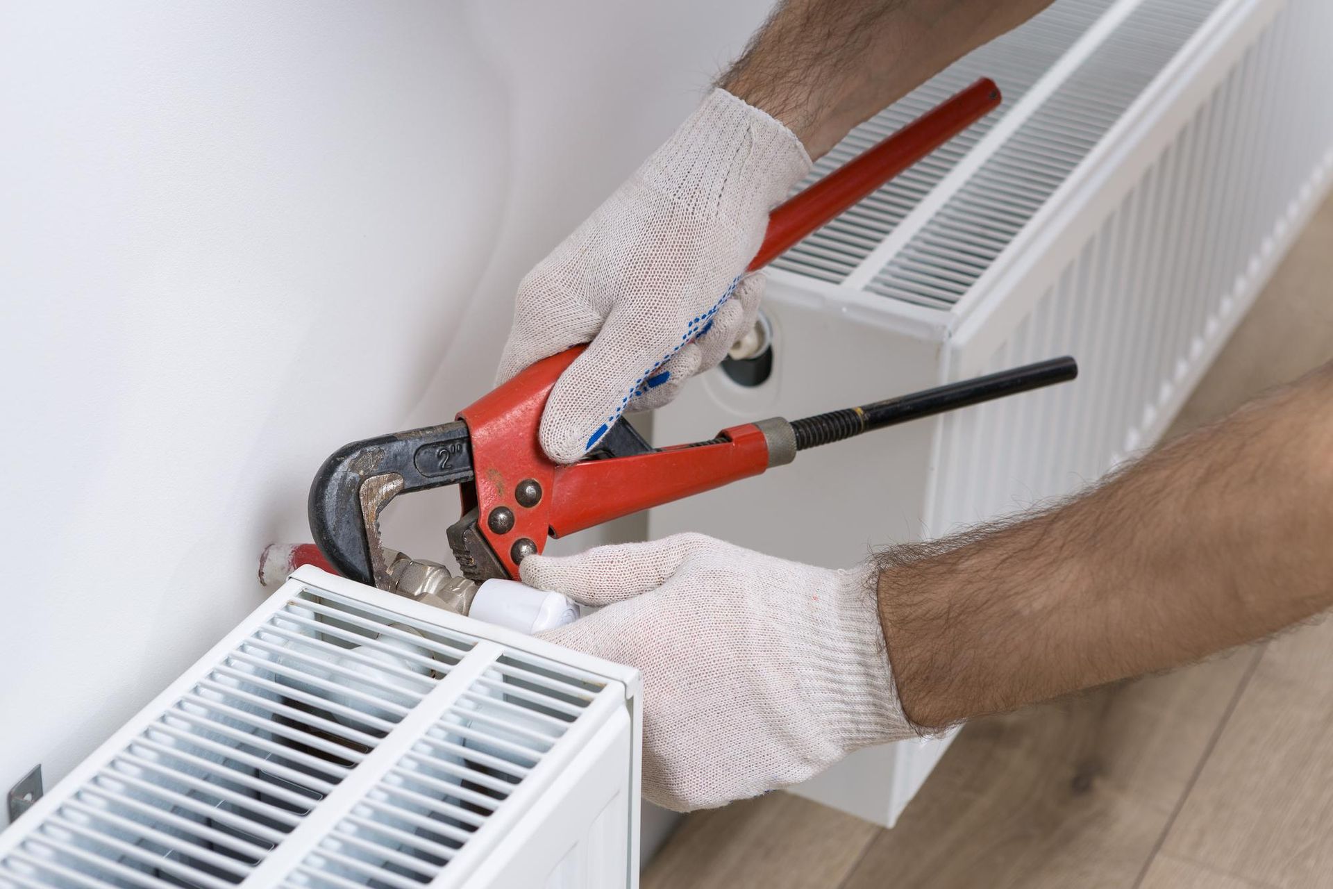 A man is fixing a radiator with a wrench.