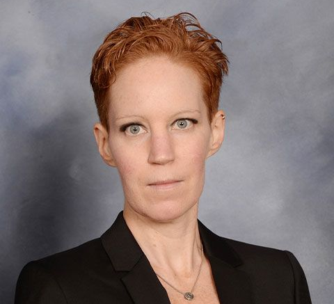 Portrait of a person in a black blazer against a gray backdrop, looking directly at the camera.