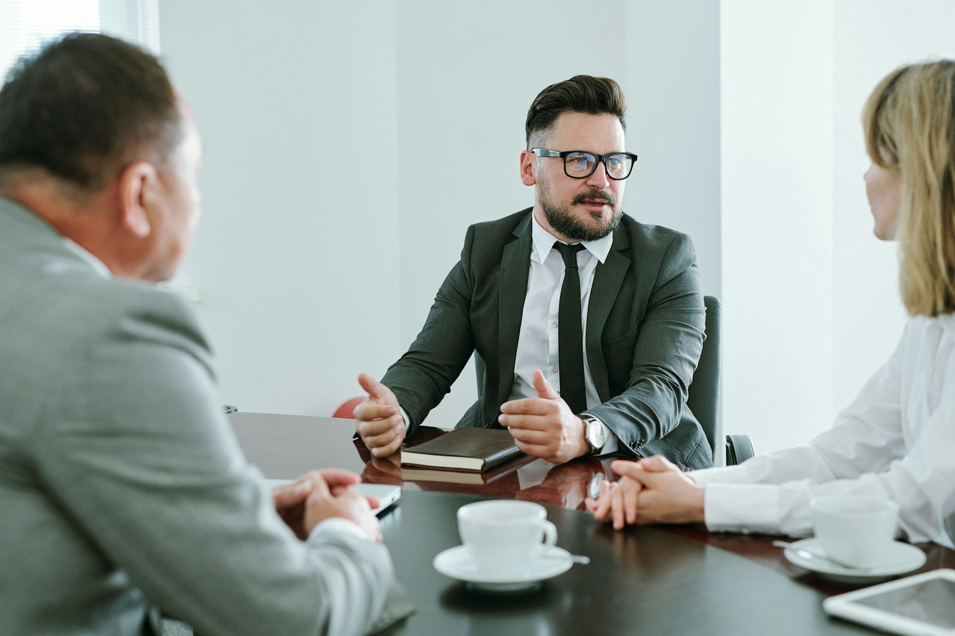 Business meeting with three people around a table, discussing papers and a laptop in a bright office.