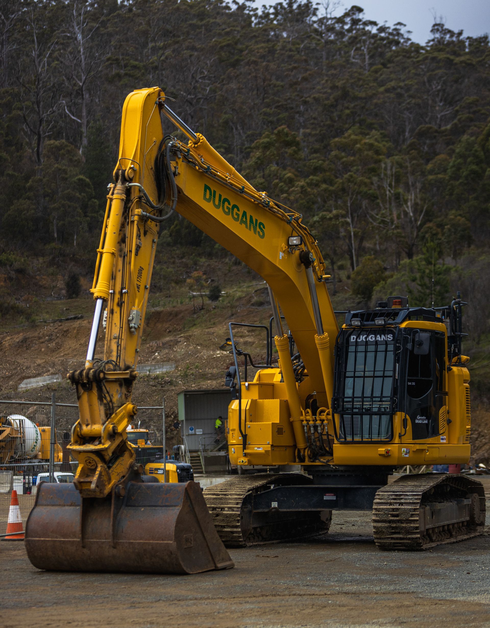 Yellow excavator with bucket on a dirt construction site, with trees in the background