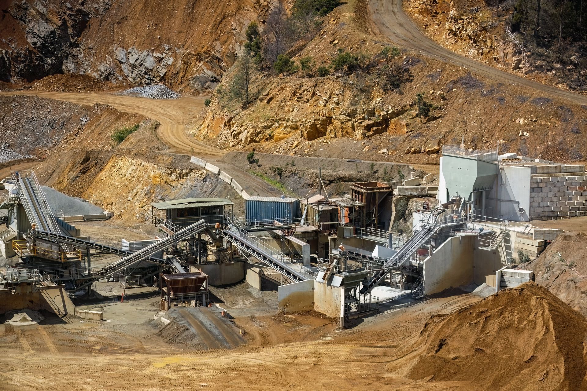 Open-pit mine with conveyor belts and industrial processing equipment on a rocky hillside.