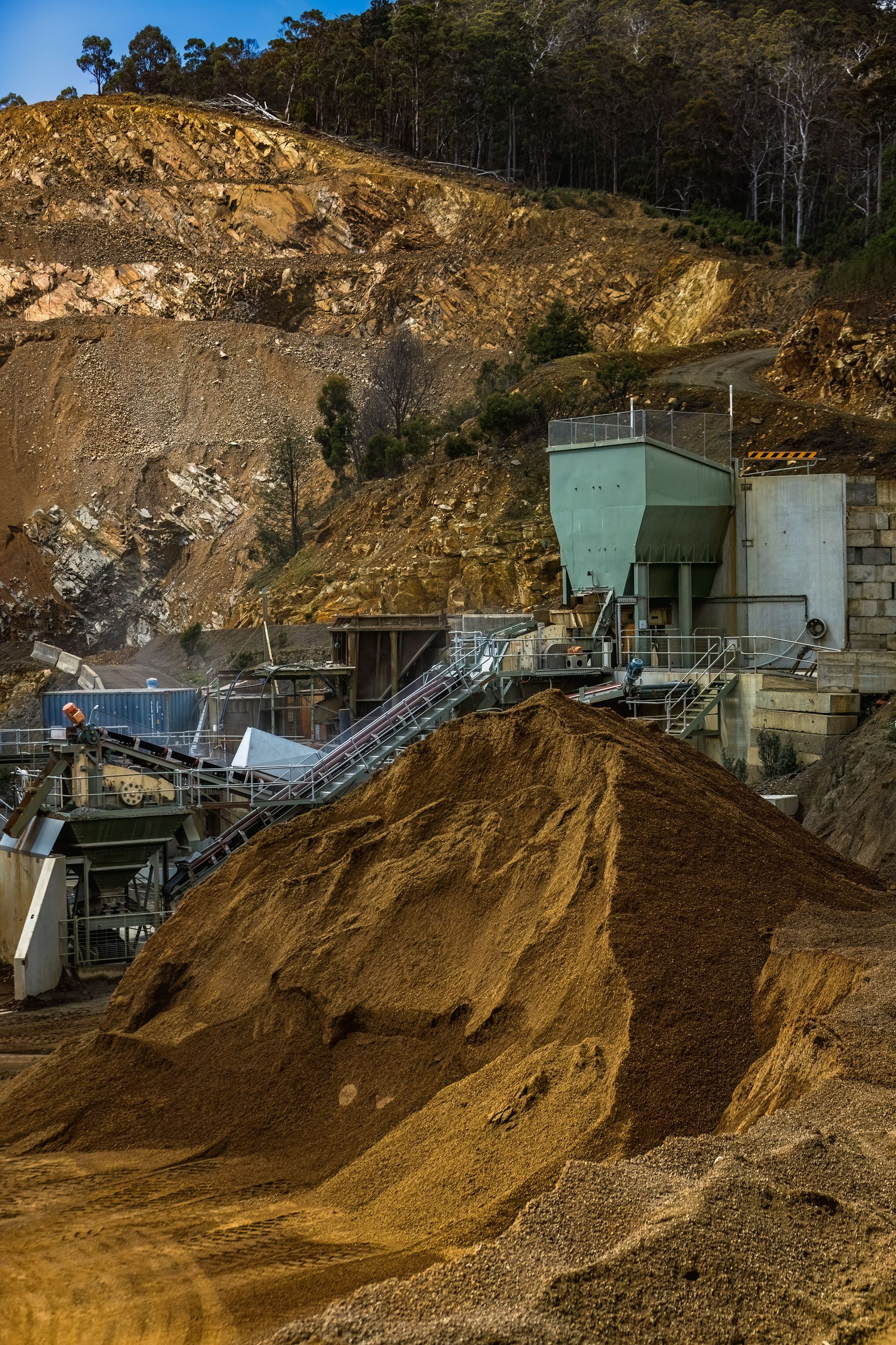 Wood chips and industrial equipment at a logging yard beside a forested hillside.