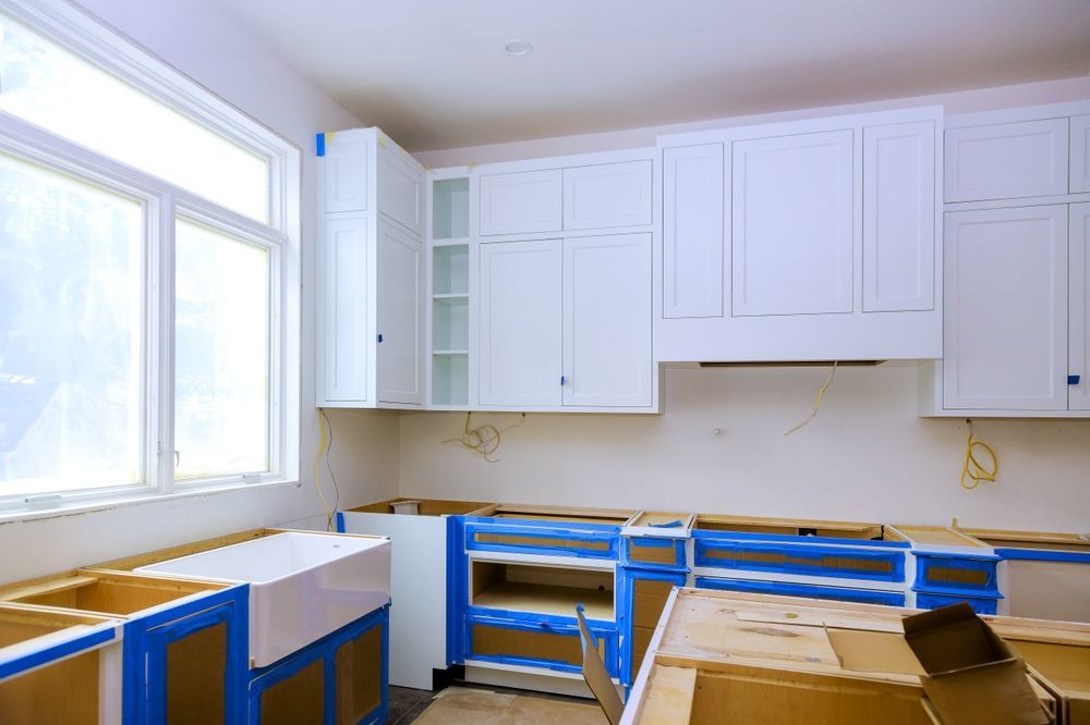 Kitchen remodel with white cabinets, blue tape, and unfinished lower cabinets near a window.