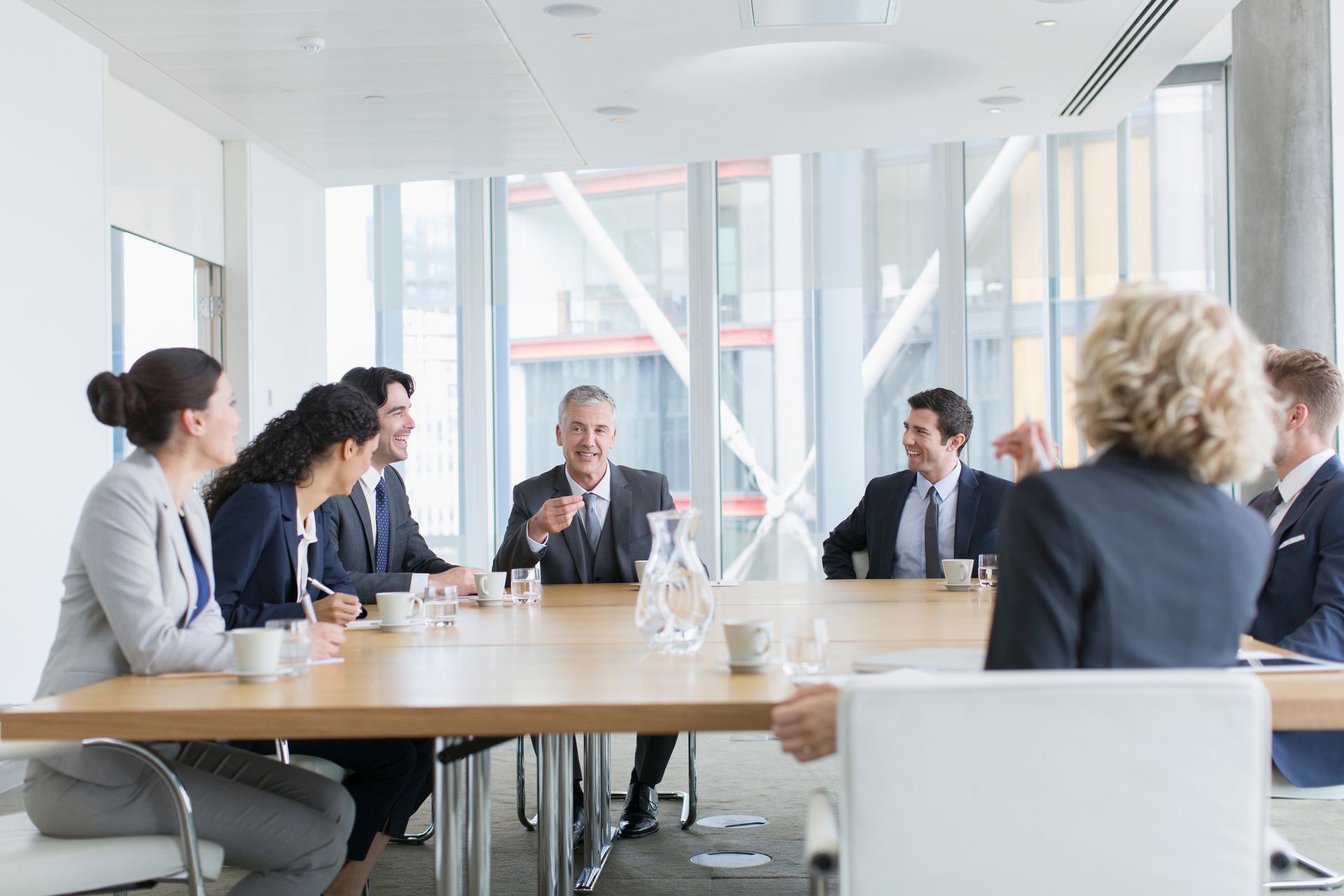 Businesspeople in suits at a conference table, discussing ideas in a bright office.
