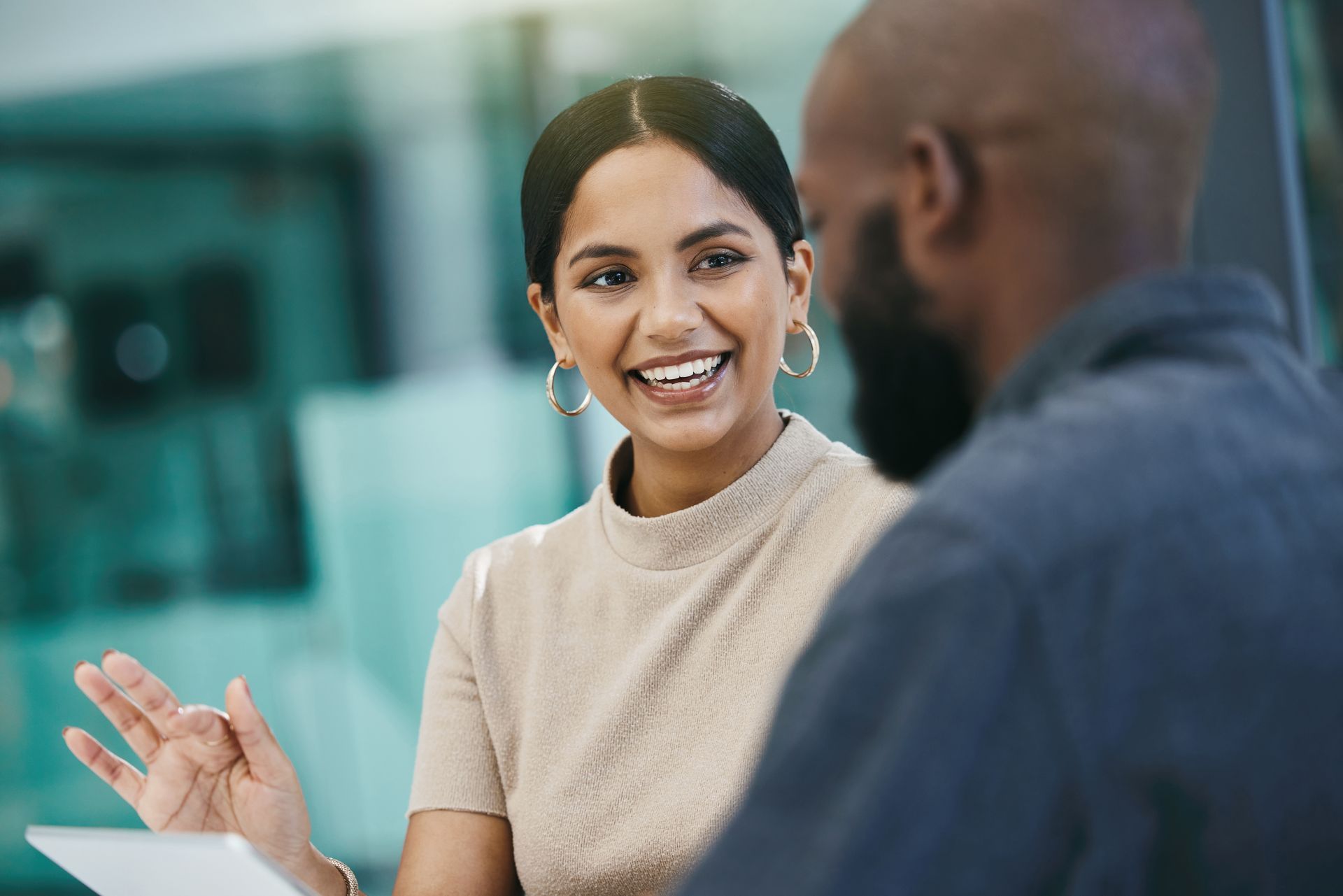 Woman smiling, gesturing, talking to a person at a table, indoors, neutral lighting.