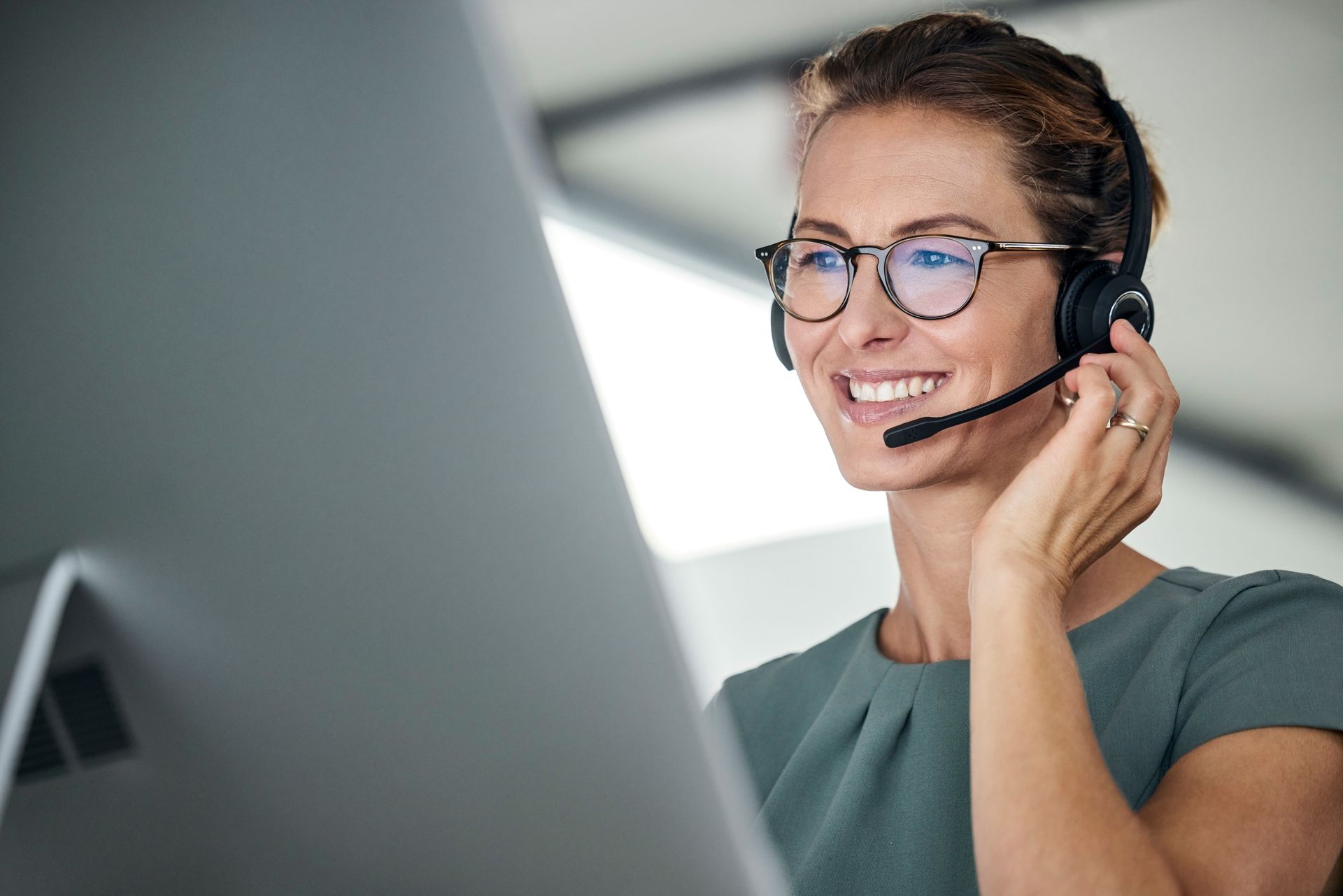Woman wearing headset smiling while looking at a computer screen.