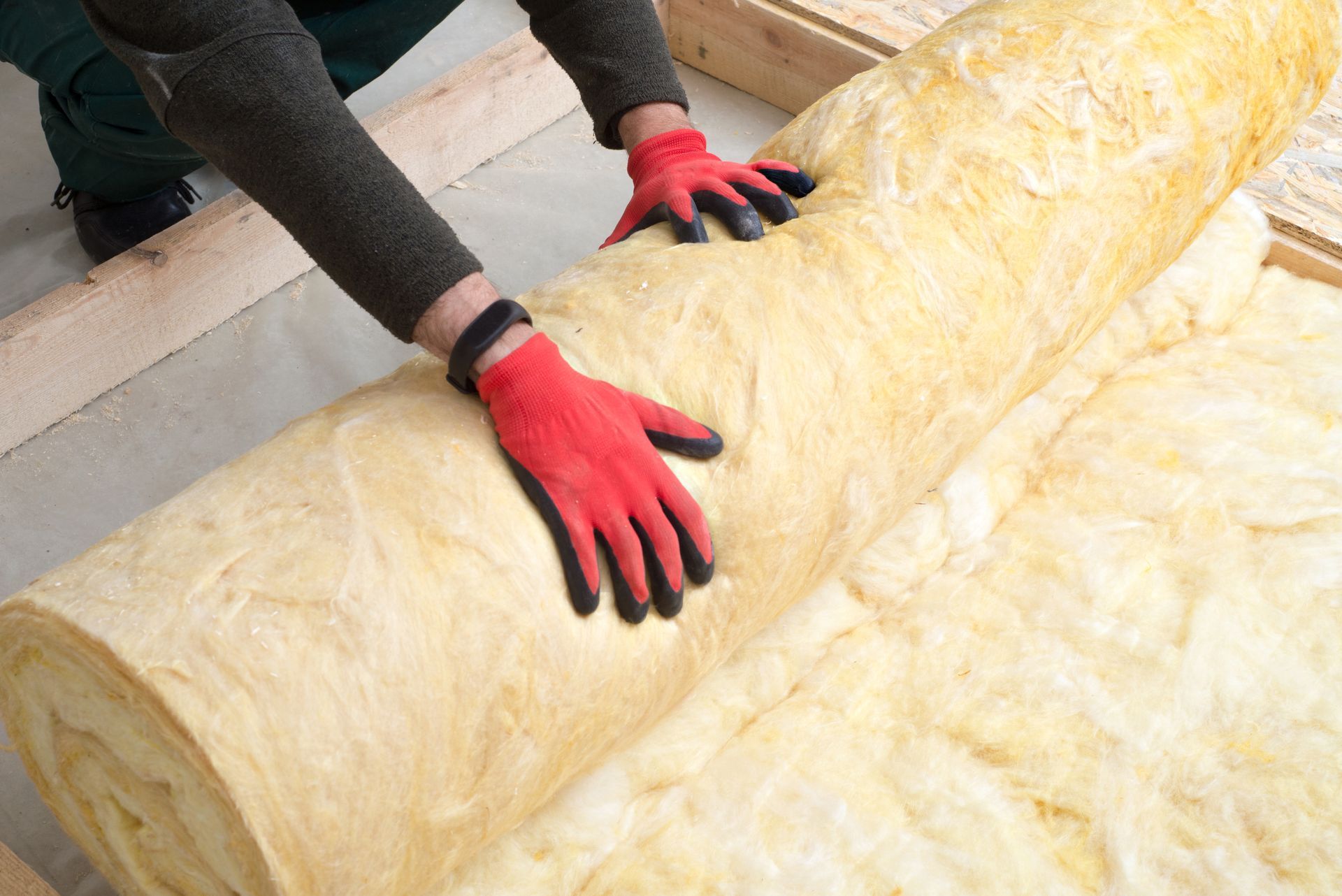 Person Rolling Out Insulation in a Building Frame, Wearing Red Gloves — Kev's Group QLD in Kawana, QLD