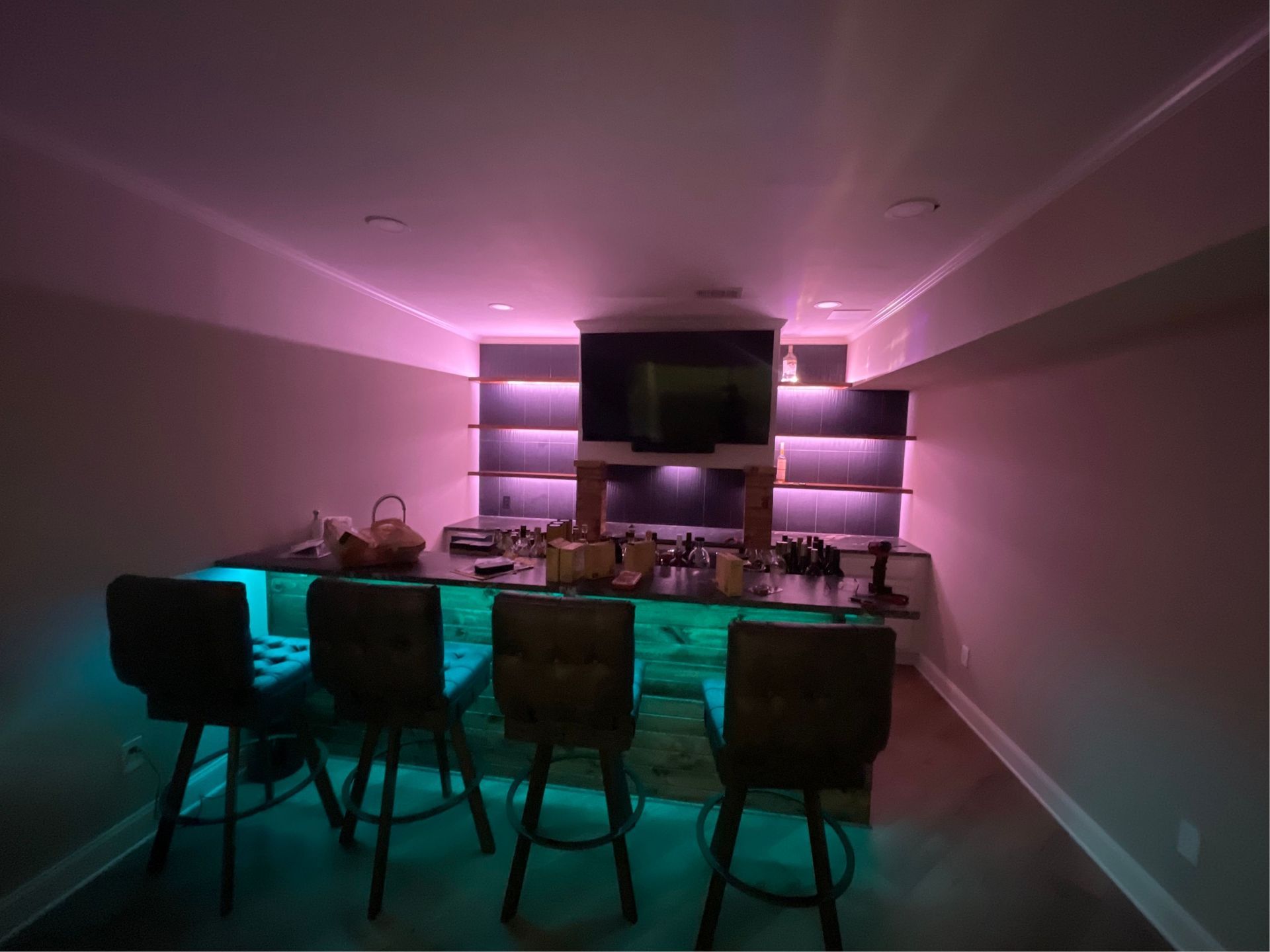 Color-changing LED accent lighting installed behind custom home bar with TV setup
