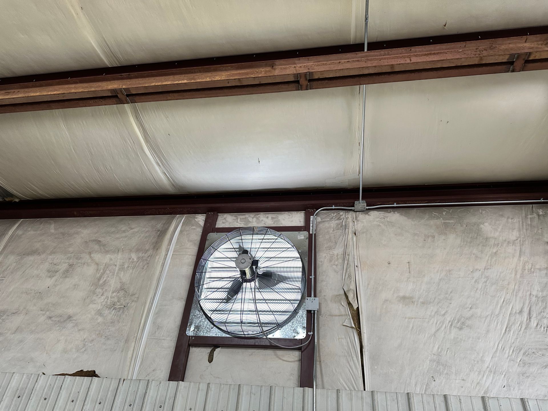 Industrial ceiling-mounted ventilation fan connected to metal conduit and support beam