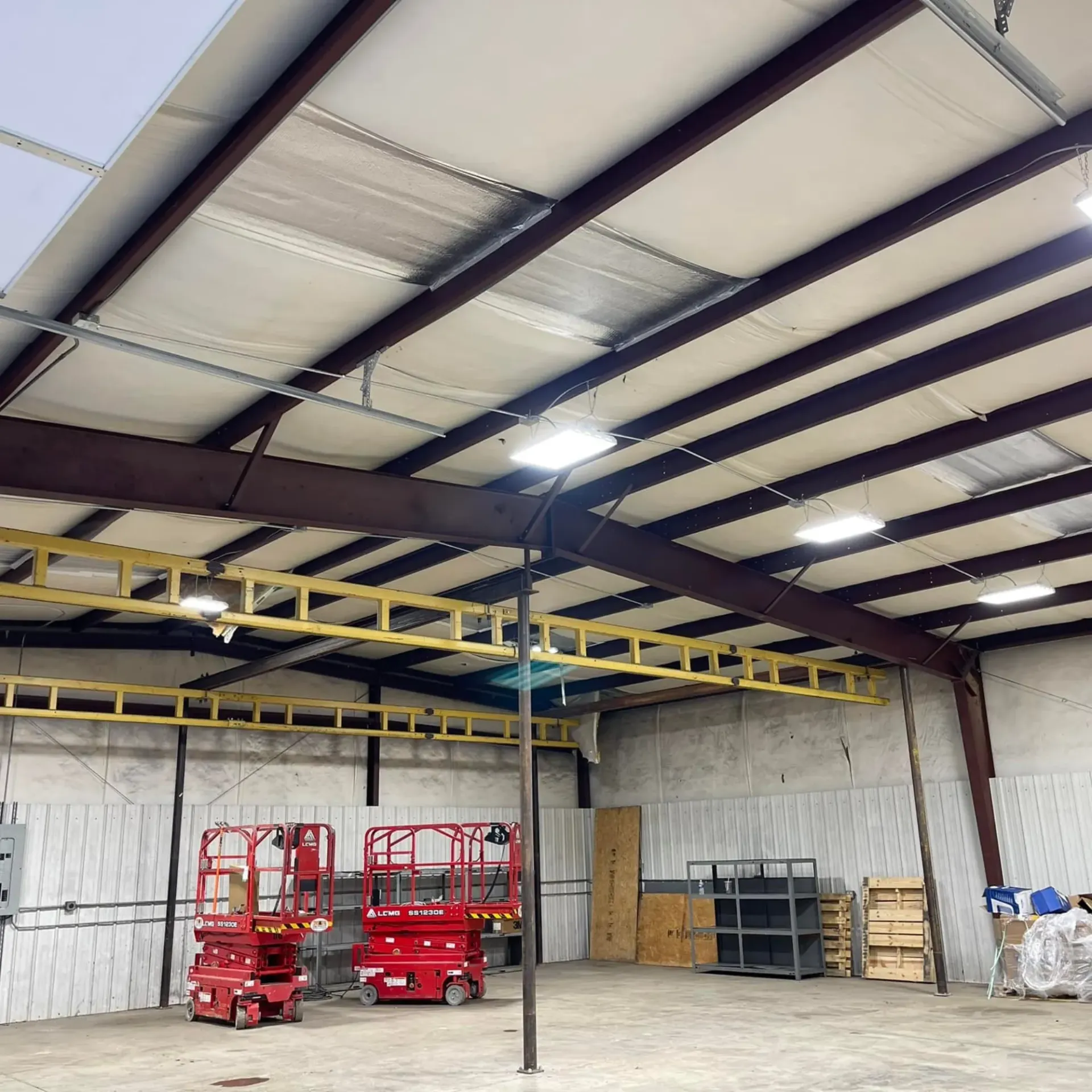 Warehouse ceiling LED lighting installation with high bay fixtures and scissor lifts