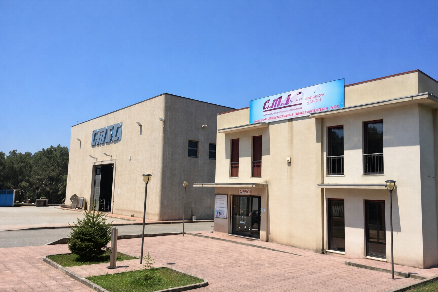 Un edificio beige a due piani con un cartello, accanto a una struttura più grande in stile magazzino, sotto un cielo azzurro.