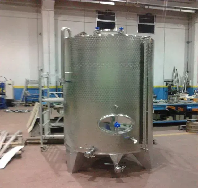 Serbatoio industriale in acciaio inox in un'officina. Cilindrico, con raccordi e base conica.