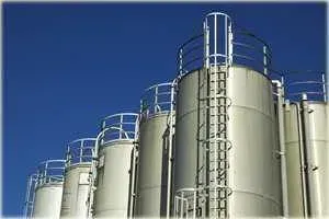 Fila di alti serbatoi industriali bianchi con scale, sullo sfondo di un cielo azzurro brillante.