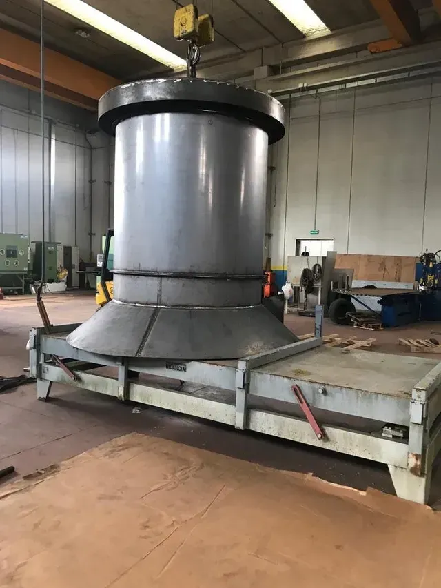 Grande componente industriale in metallo sospeso da una gru all'interno di una fabbrica.