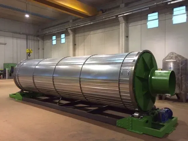 Grande essiccatore a tamburo industriale in acciaio inossidabile su supporti verdi in un magazzino.