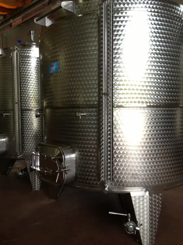 Serbatoi per vino in acciaio inossidabile in una cantina vinicola. Cilindrici, strutturati e dotati di porte di accesso.