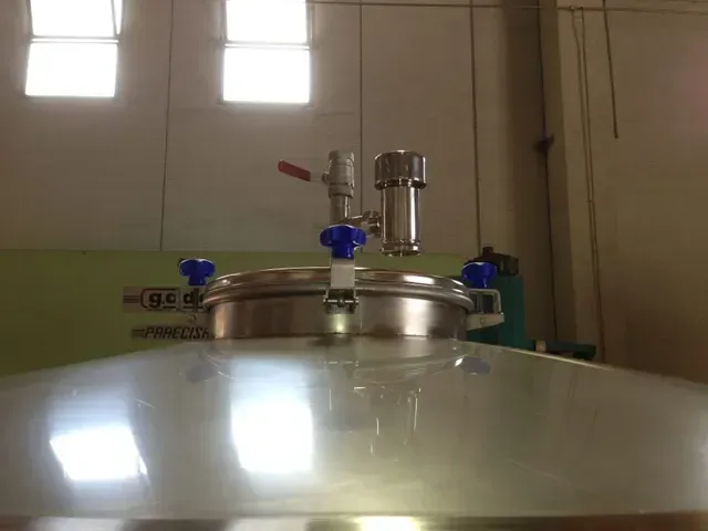 Coperchio per serbatoio in acciaio inox con valvole, ambiente industriale.