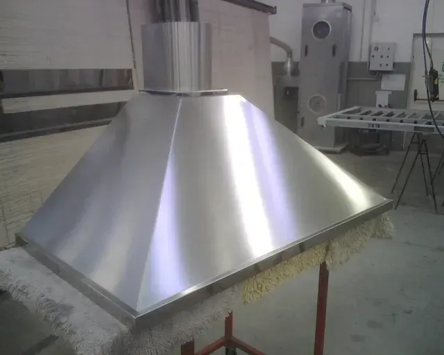 Cappa aspirante commerciale in acciaio inox su banco da lavoro, con tubo di ventilazione.