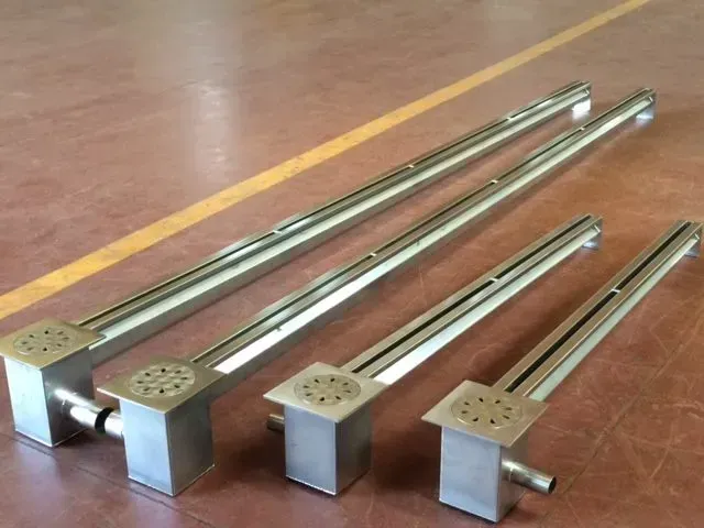 Quattro scarichi lineari per doccia in acciaio inossidabile di diverse lunghezze, posizionati su un pavimento marrone.