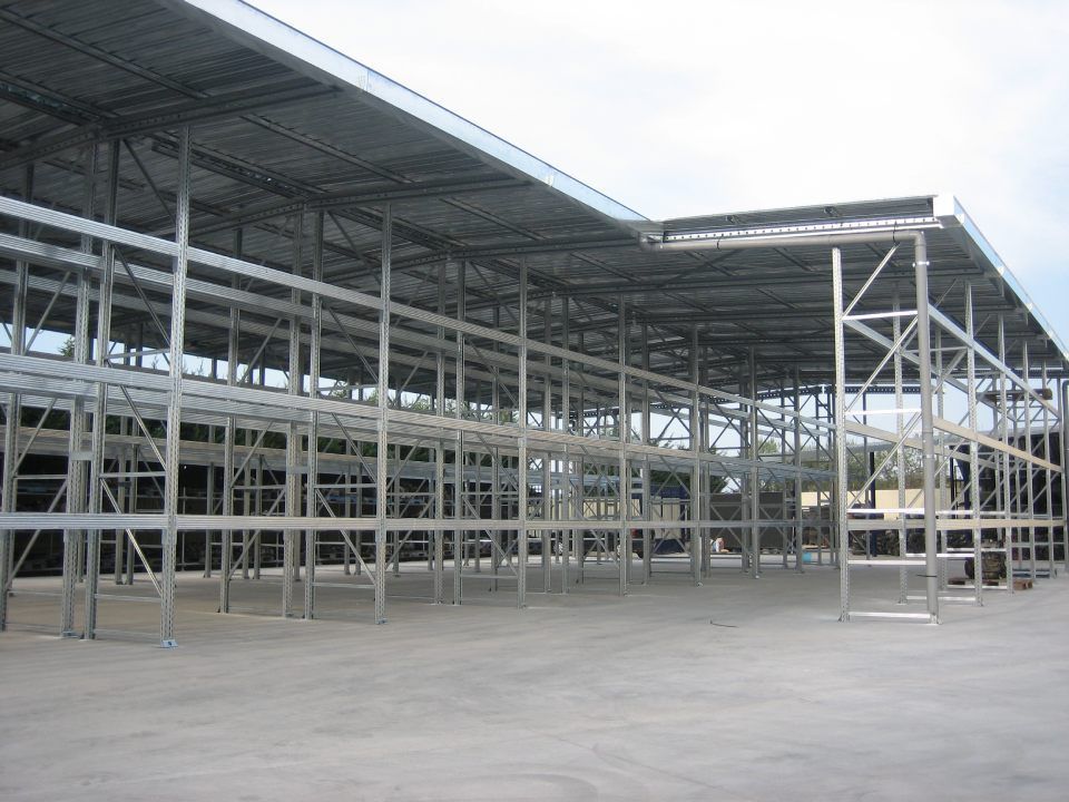 Struttura metallica di un grande edificio industriale, con tetto piano, lati aperti e pavimento in cemento.