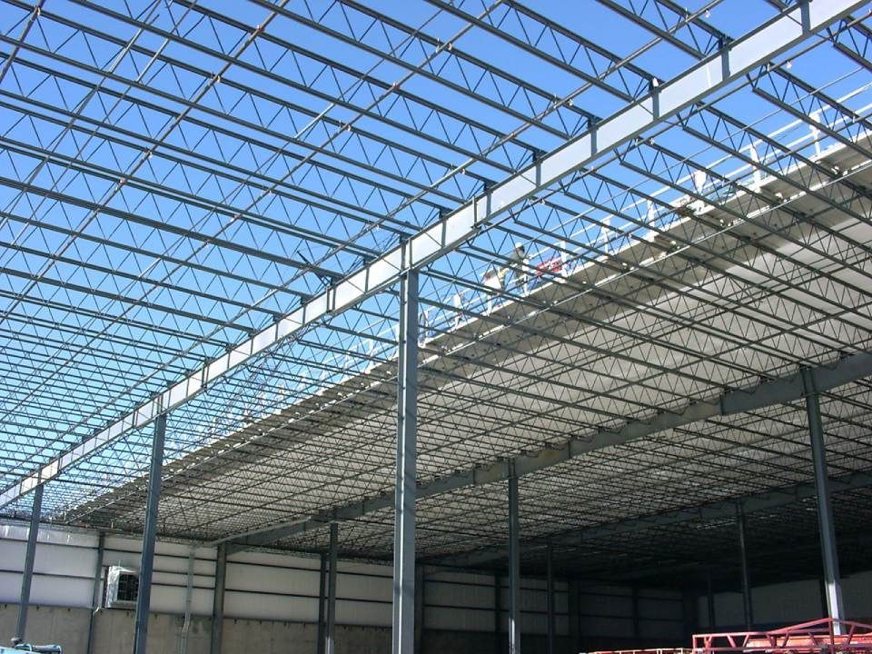 Struttura metallica del tetto di un magazzino, con travi e capriate in acciaio contro un cielo blu.