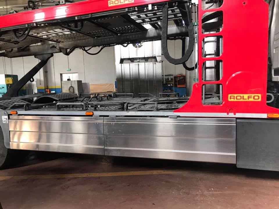 Vista laterale di un camion per il trasporto di automobili rosso e argento in un garage.