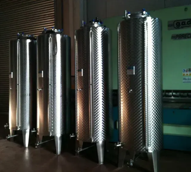 Quattro serbatoi industriali in acciaio inossidabile in un magazzino.