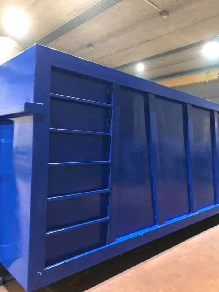 Cassonetto industriale blu con struttura a forma di scala su un lato, all'interno, probabilmente in una fabbrica.