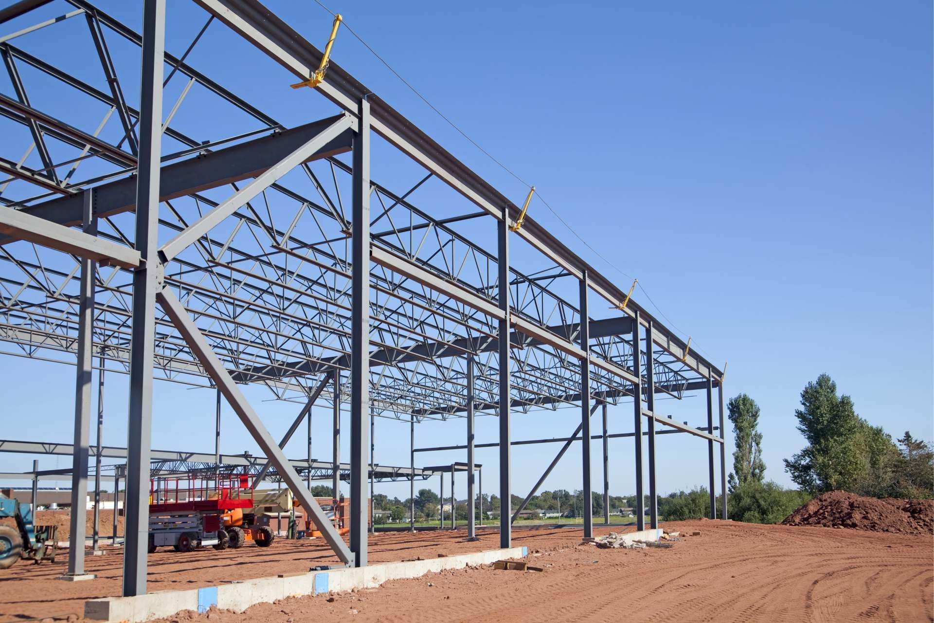 Struttura in acciaio di un edificio sotto un cielo azzurro, su un terreno di terra rossa.
