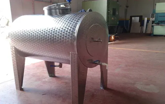 Serbatoio di fermentazione del vino in acciaio inossidabile con superficie strutturata e rubinetto su pavimento in cemento.