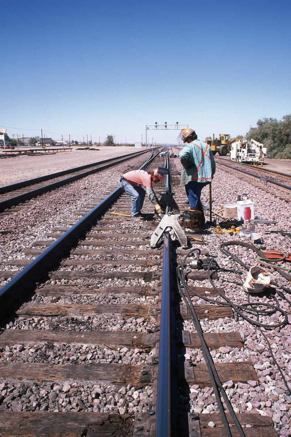Gli operai riparano i binari ferroviari in una giornata di sole. Due uomini in abiti da lavoro usano gli attrezzi sui binari.