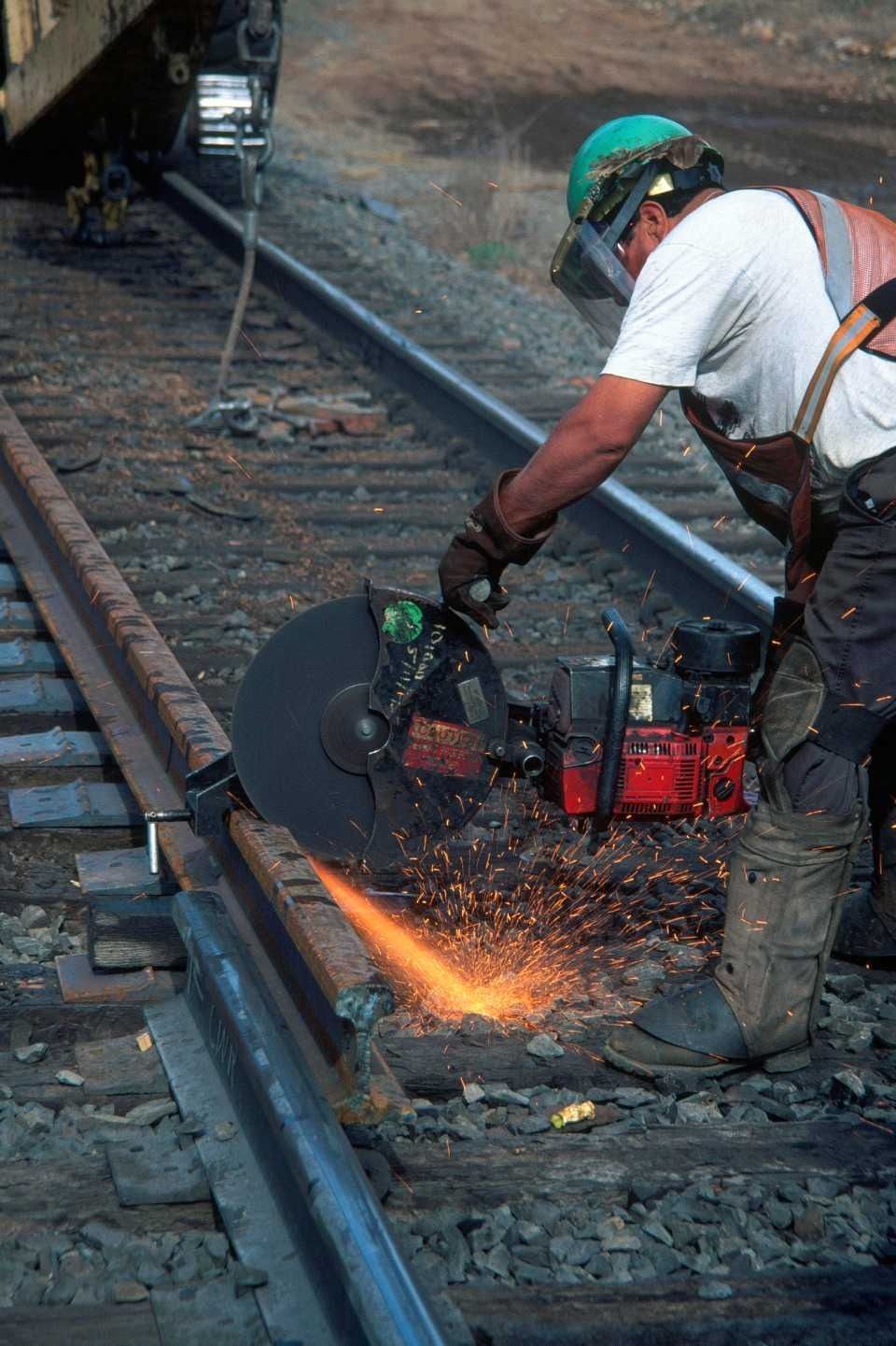 Un ferroviere usa una sega circolare per tagliare una rotaia. Scintille che volano mentre lavora in un ambiente ferroviario.