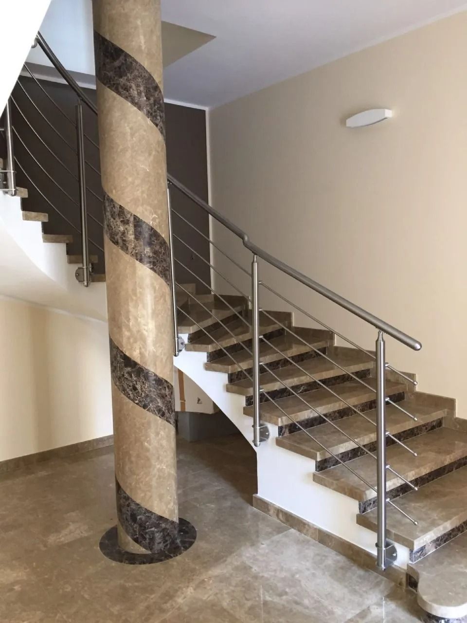 Scala con gradini in marmo, corrimano in acciaio inox e colonna decorativa con motivo a spirale.