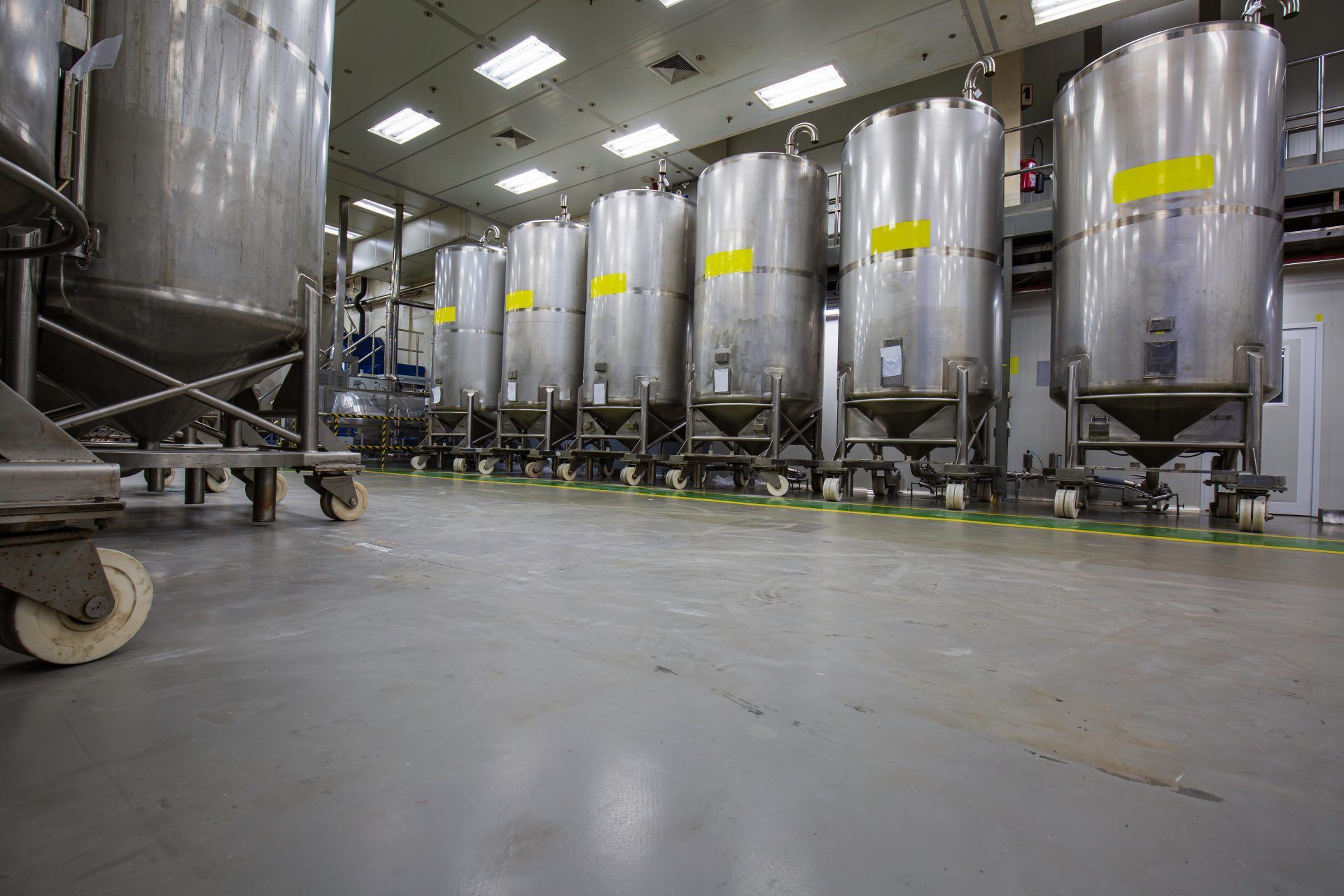 Fila di grandi cisterne industriali argentate su ruote, all'interno di una fabbrica.