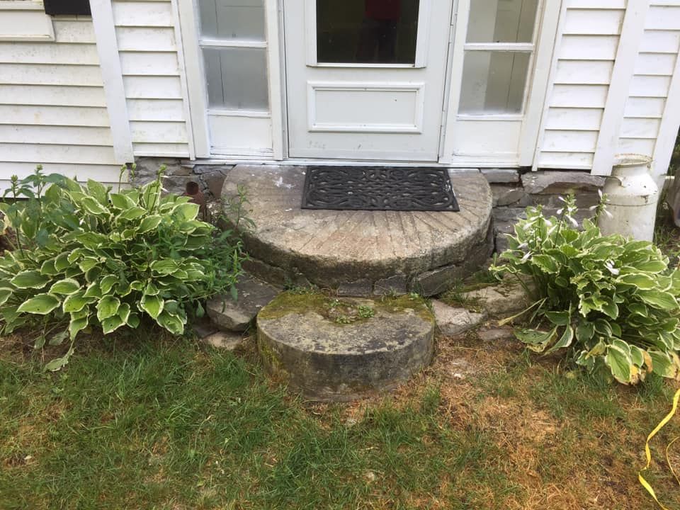 A black door mat sits on a stone step in front of a white house