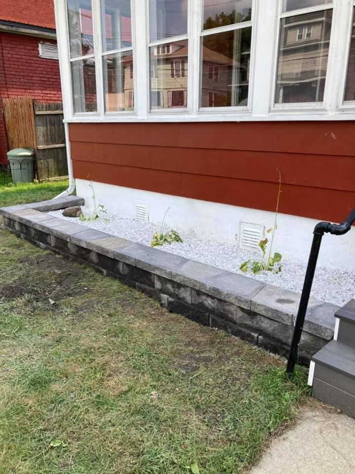 The side of a house with a stone wall and gravel in front of it