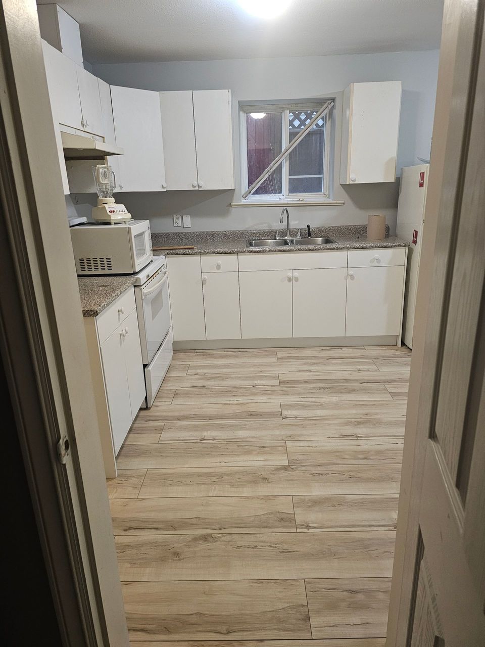 A kitchen with white cabinets and a wooden floor.