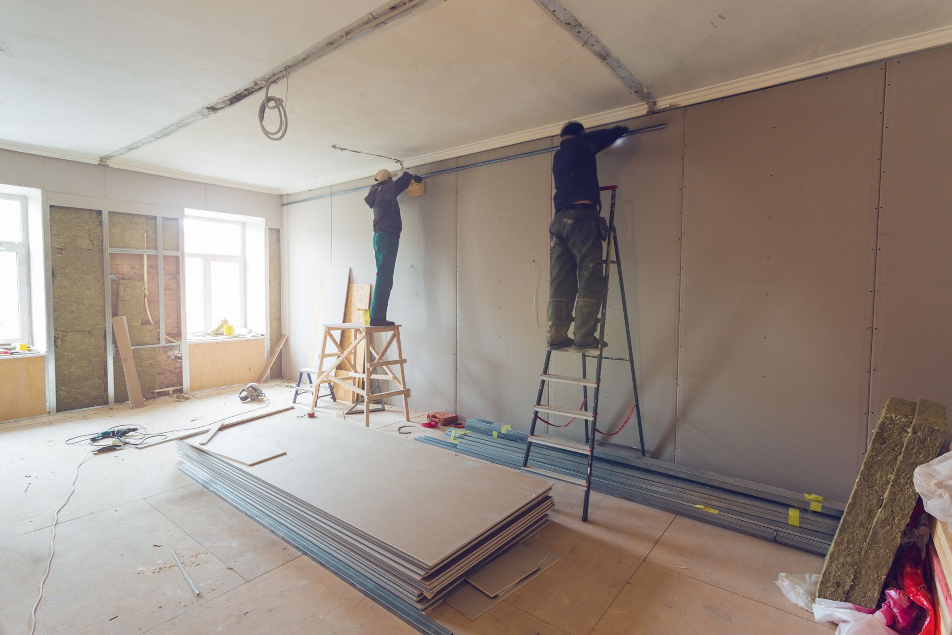 Two men are working on a wall in an empty room