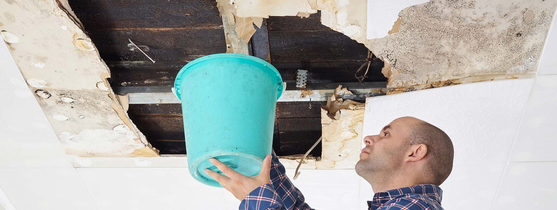 A man is holding a blue bucket over a hole in the ceiling