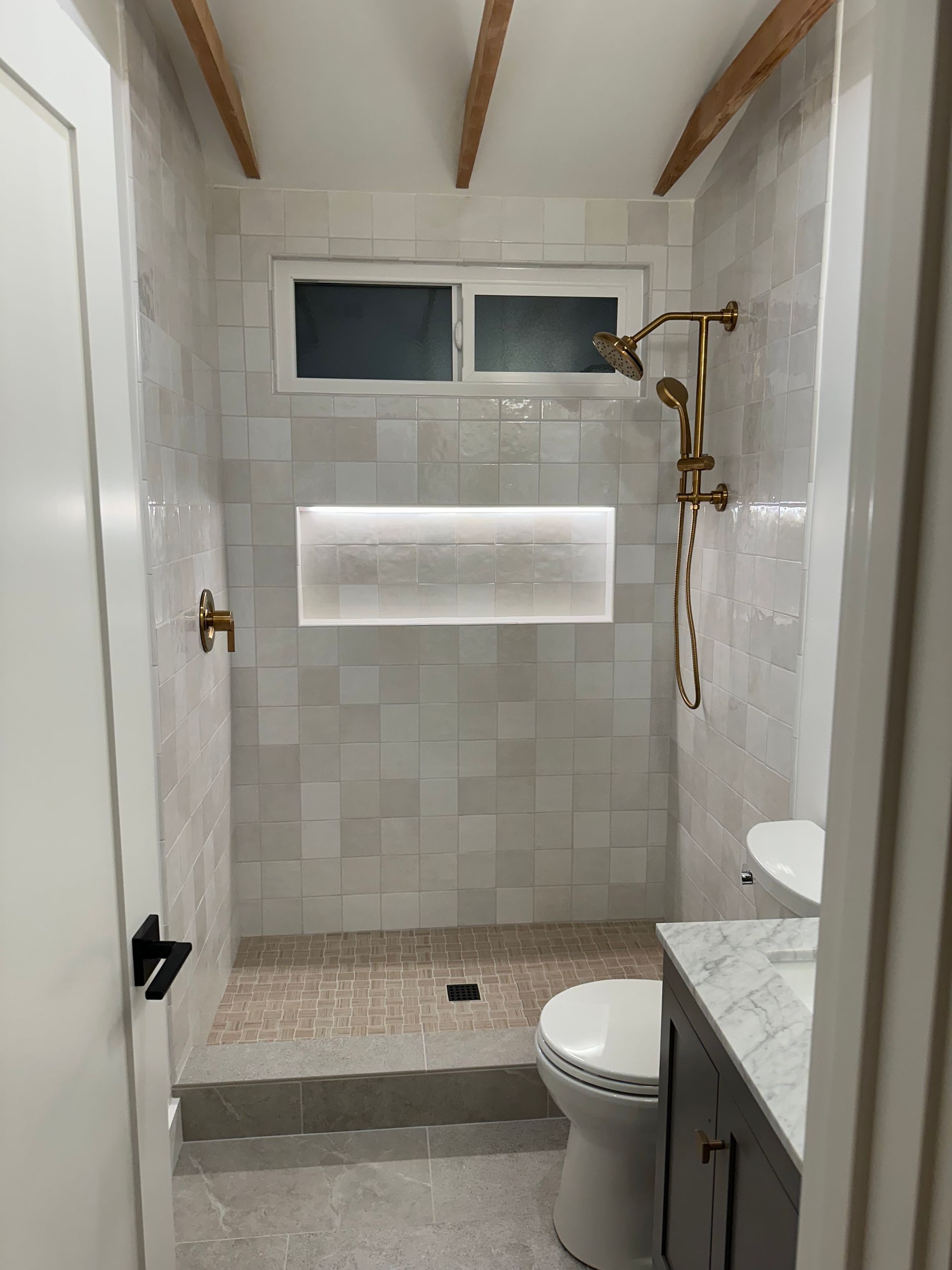 A bathroom with a walk in shower , toilet , sink and window.