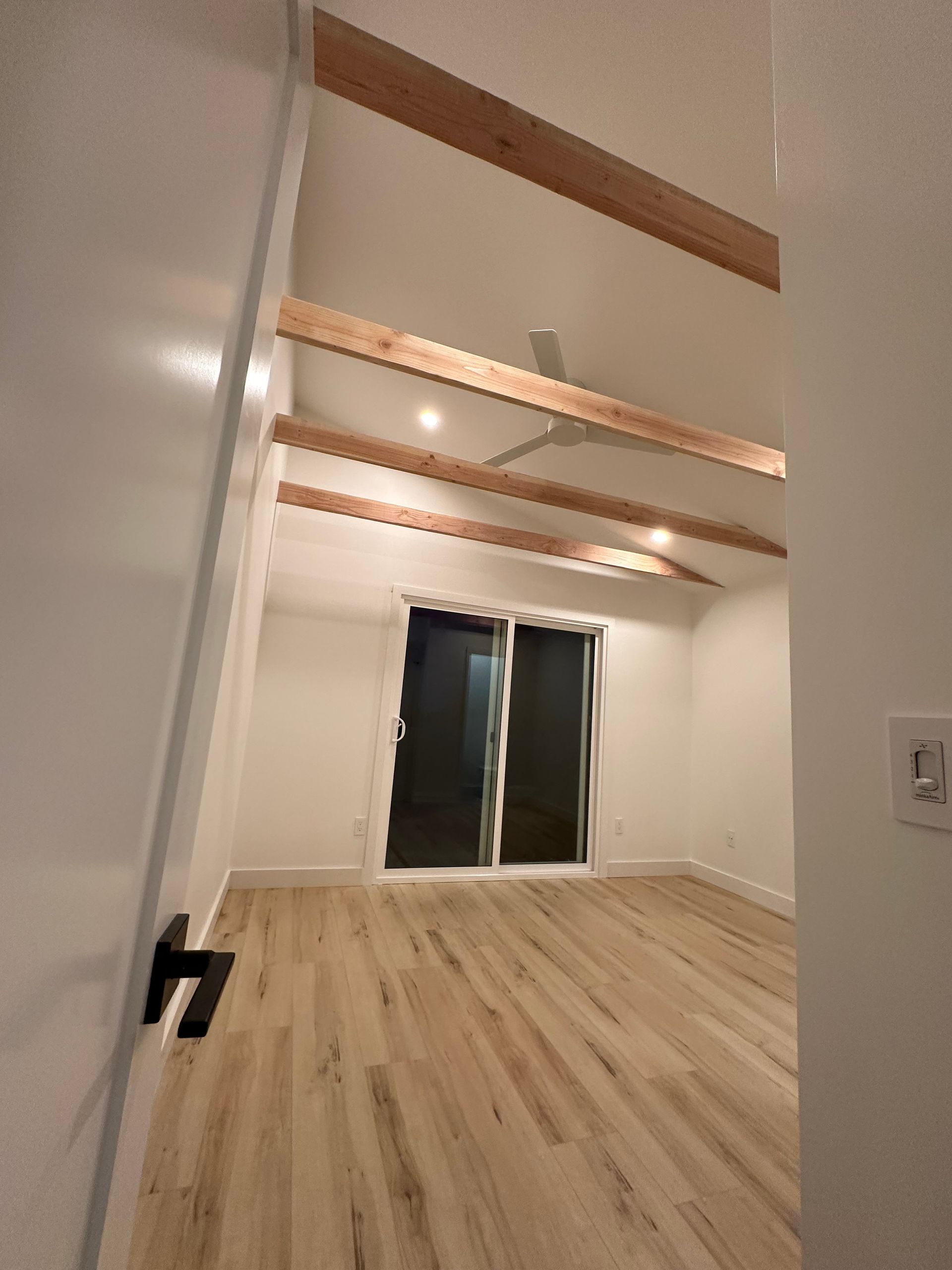 An empty room with wooden beams and a ceiling fan.