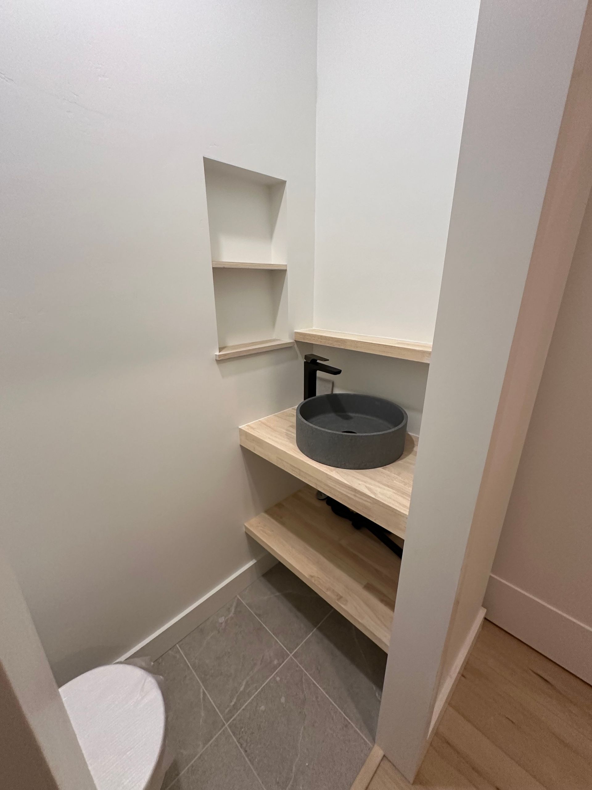 A bathroom with a toilet , sink and shelf.